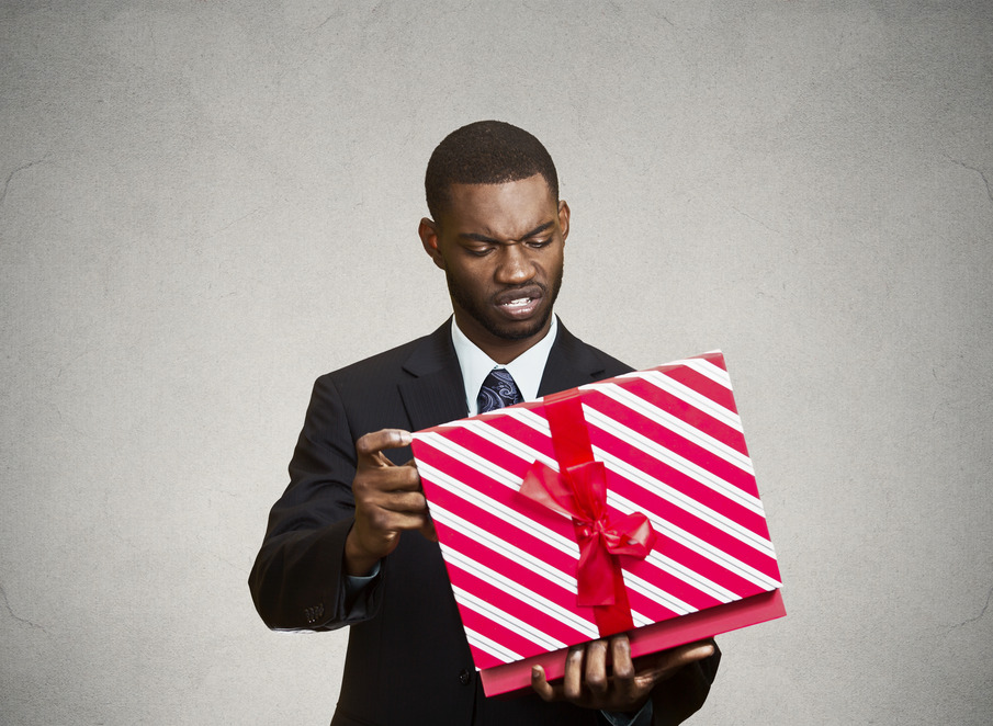 Closeup portrait grumpy, unhappy, upset man holding box, displeased with received gift, disgust on face, isolated grey black background. Negative human emotion, facial expression, feeling attitude