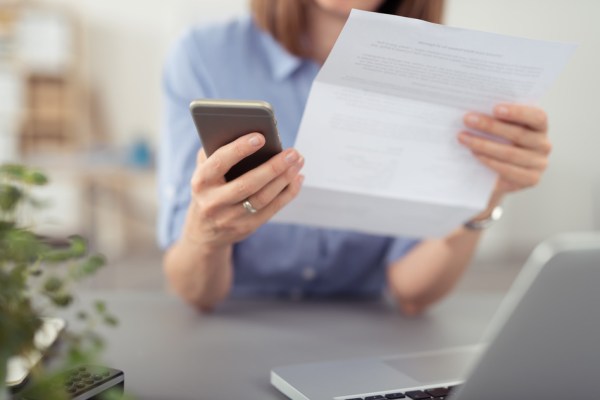 Businesswoman making a call on her mobile concerning a paper document she is holding in her hand, close up view