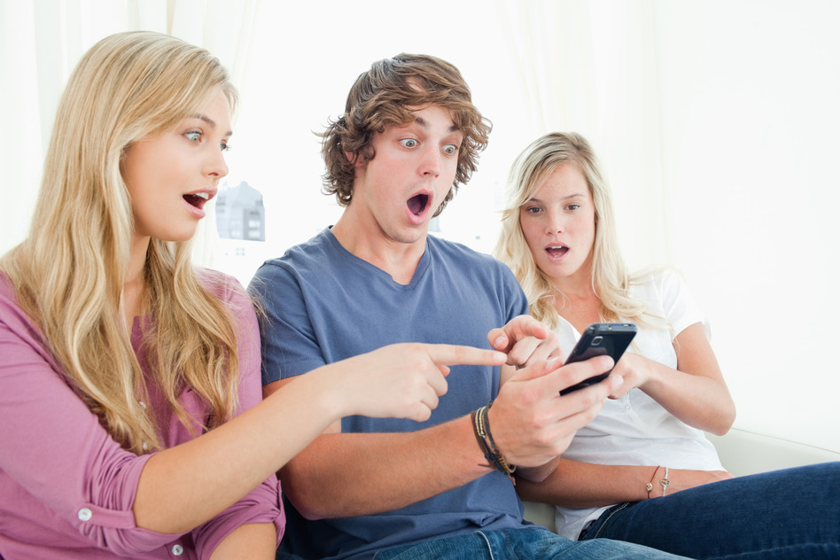 Three friends sitting on the couch as they look at the message on their phone in shock