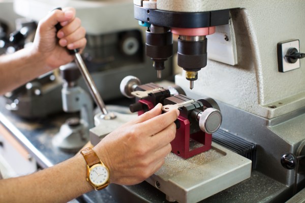 Keymaker cutting duplicates of keys on laser machine at workshop