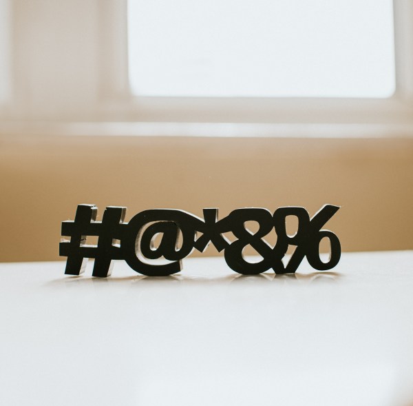 Conceptual and simple image of special characters, # @ * & % on a white table, with a plain background, casting shadow. These characters are often used in auto-generated passcodes and passwords. Surface provides a space for copy.