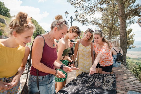 Small group of people are crowded round a jewellery stall in Volterra, choosing products to buy.