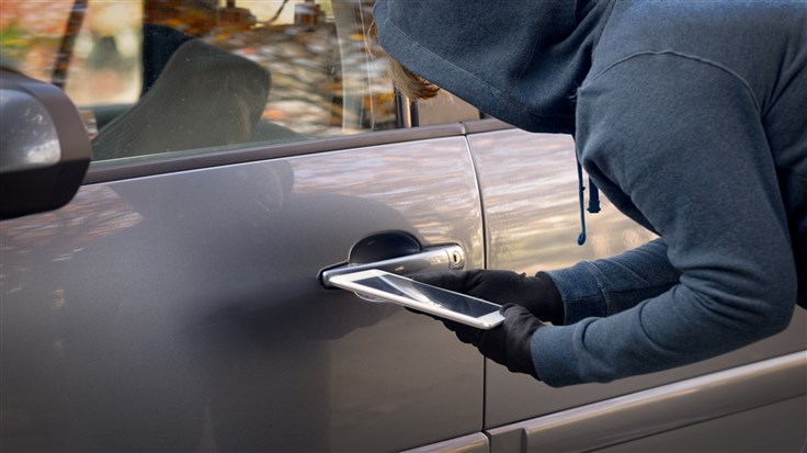 Hooded thief tries to break the car's security systems with tablet. Hacking modern car concept