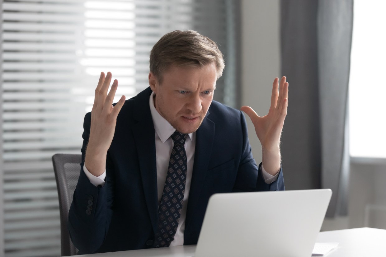 Annoyed mad businessman wearing suit frustrated with online problem, angry stressed male professional using laptop outraged by broken pc, crazy about stuck slow computer virus app error at workplace