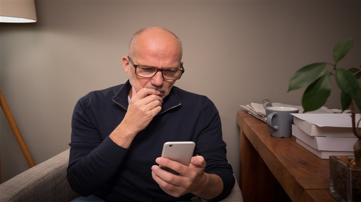 Mature man at home using smartphone for online banking, shopping, social media, e-mail, etc. The serious expression indicates there's something to think about ... phishing, e-mail scam, online abuse, identity theft, who knows what?