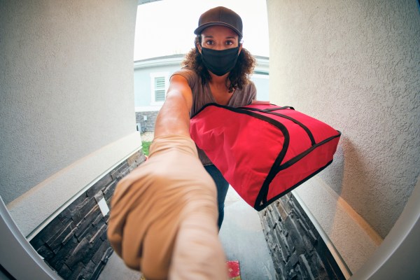 A young woman delivering takeout food to a home in the evening.