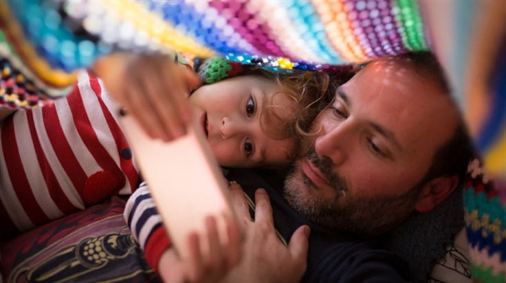 father and daughter watching on phone under a blanket