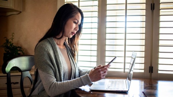 A woman looking at her phone and laptop