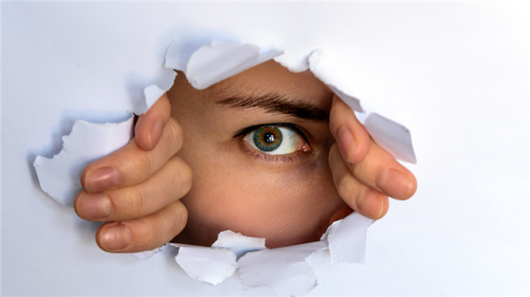 eye peeking thorugh a hole in paper