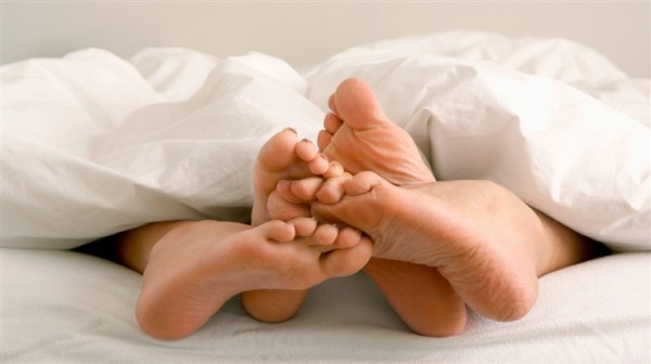 couple’s feet touching each other while under the duvet