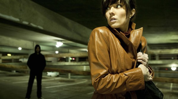 woman followed by a figure in the shadows in a parking garage