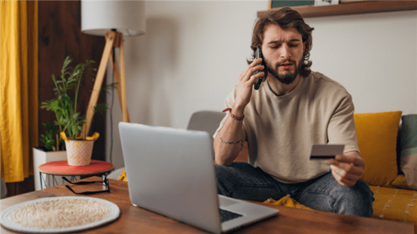person looking at his credit card and his laptop while on the phone