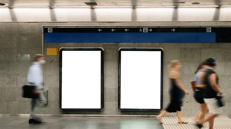 People walk past blank advertising frames hung up in a subway station