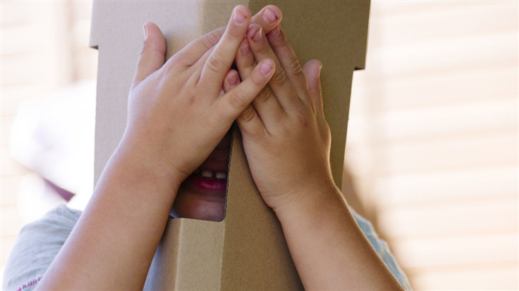 child hiding behind cardboard mask