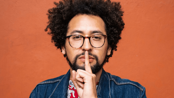 Man holding his finger to his lips to indicate secrecy.