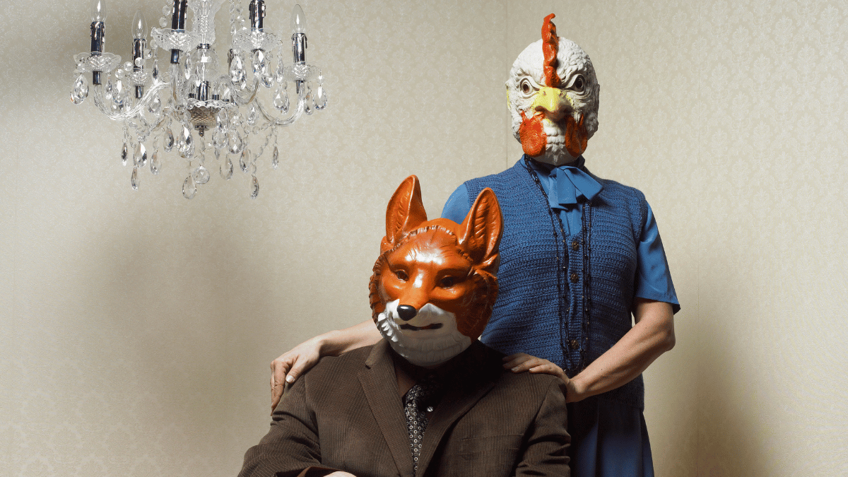 A couple wearing a chicken and a fox mask.