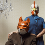 A couple wearing a chicken and a fox mask.