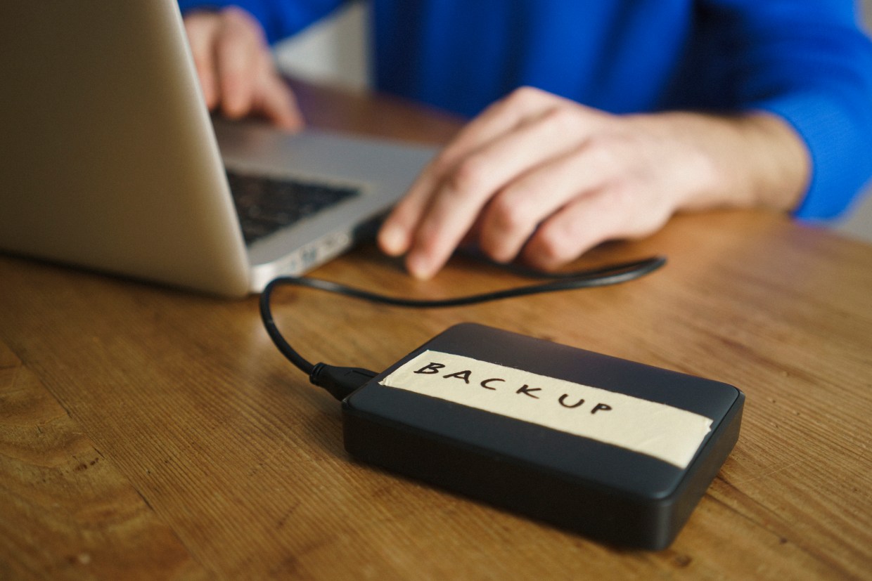 An external storage device that has the label "backup" is connected to a Macbook computer