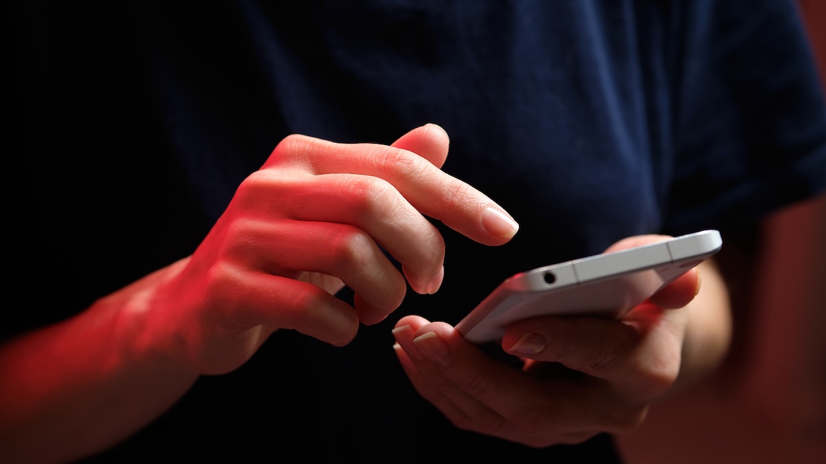 A mobile phone in the hands of a young woman in a dark colored t-shirt.
