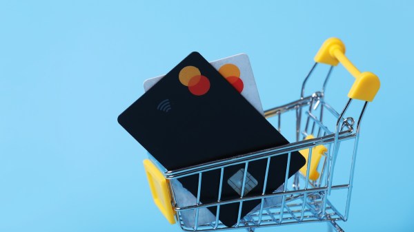 A tiny shopping cart carries two credit cards. It rests in front of a light blue background.
