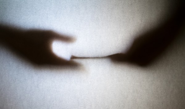 Behind a semi-opaque screen, one person's hand passes cash secretly to another person's hand