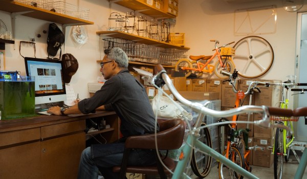 A man manages his online web business as he sits amongst his inventory of bicycles and accessories