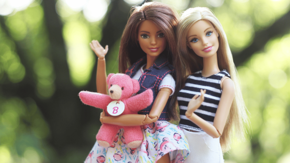 Two Barbie dolls holding a teddy