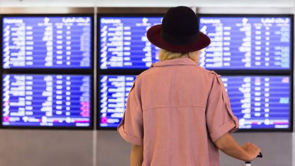 A woman stands in front of a timetable that includes information about departing and arriving flights