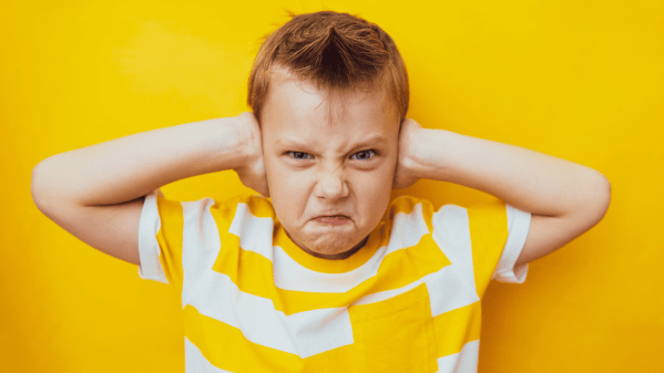 Young boy covering his ears on a yellow background
