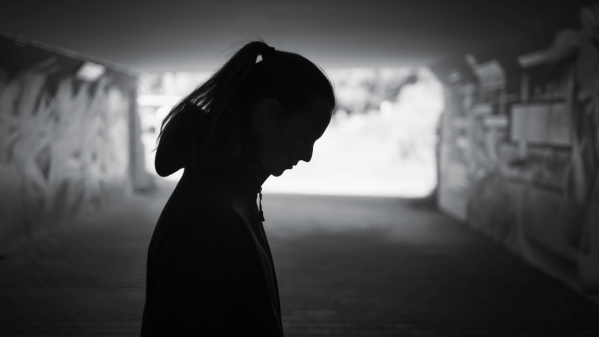 Silhouette of woman in underpass looking down at the ground