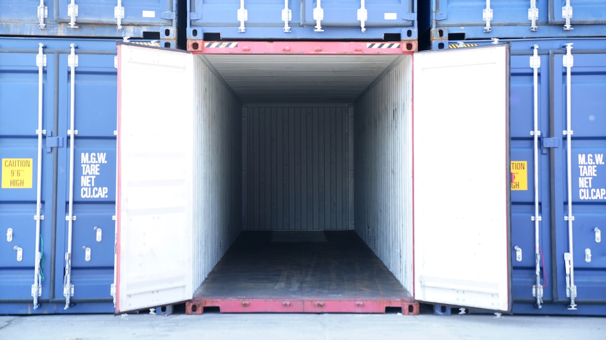 A cargo container is opened up amidst other containers. It is entirely empty.