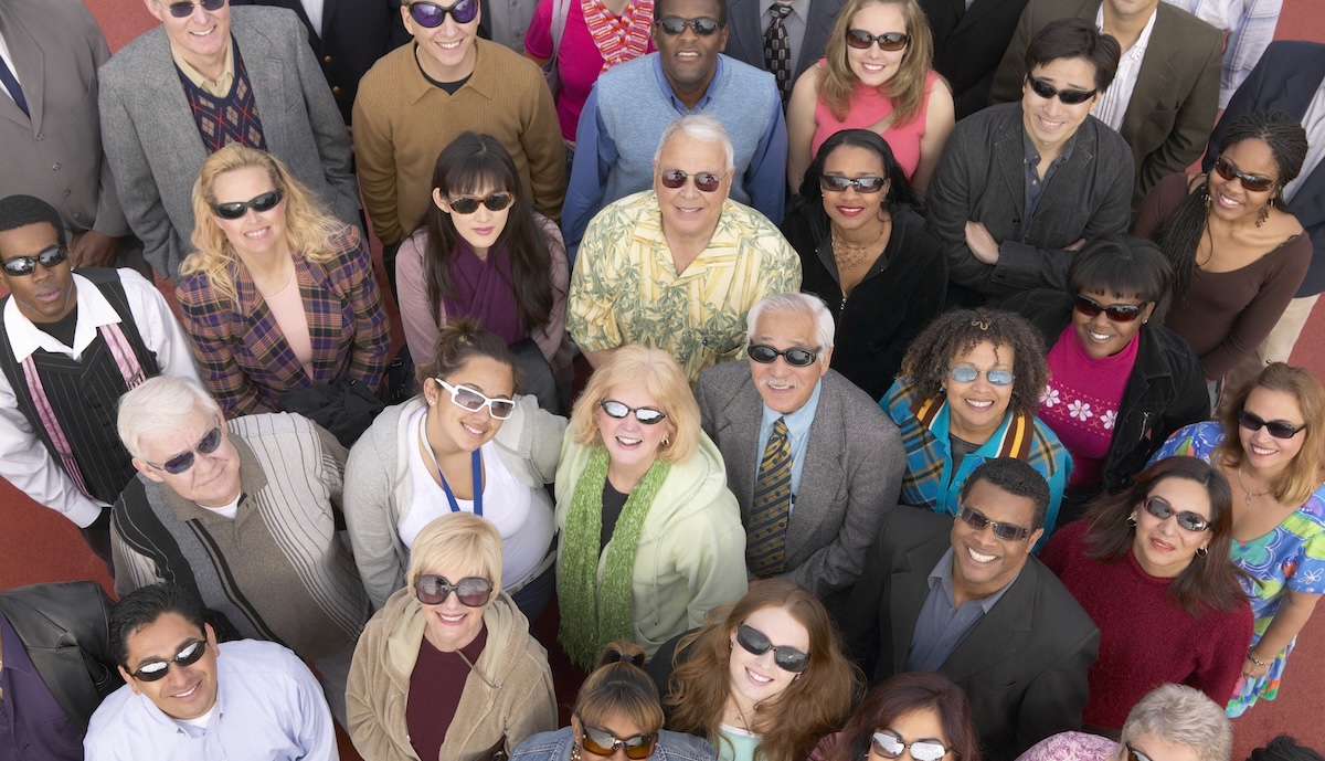 A group of people wearing a variety of sunglasses looking up at the sky and into the camera