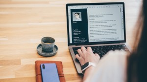 A woman searches for a job on her laptop, her resume visible on the screen
