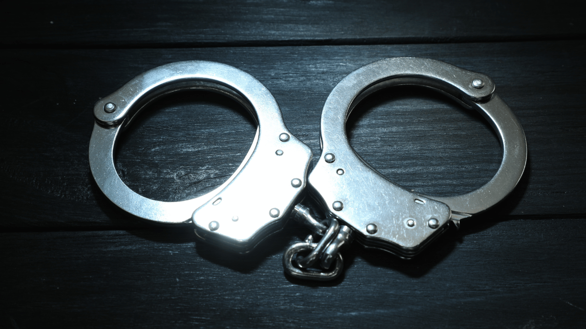 A pair of metal handcuffs on a black, wooden surface